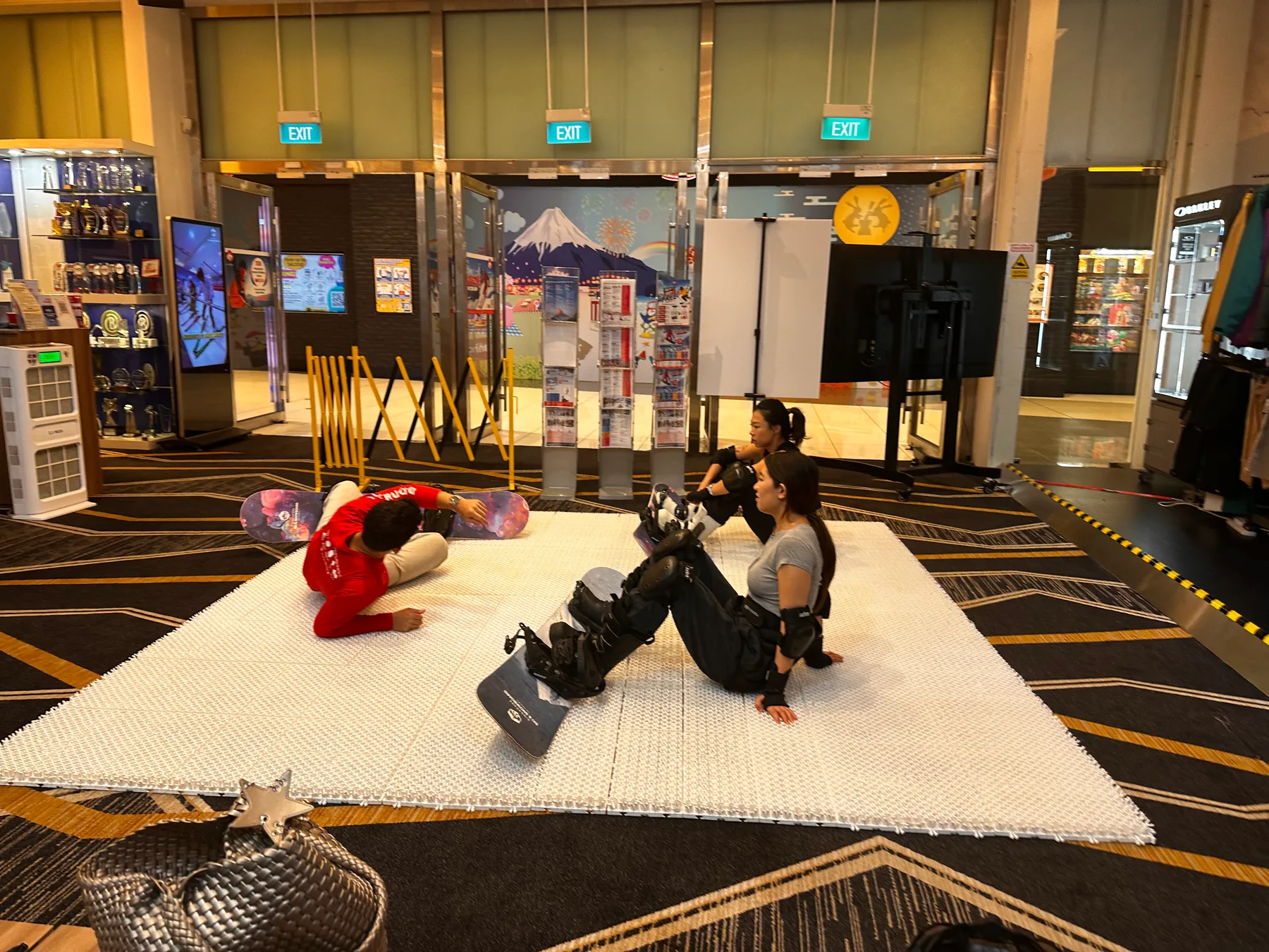 Three snowboarders resting with their boards beside the indoor training slope