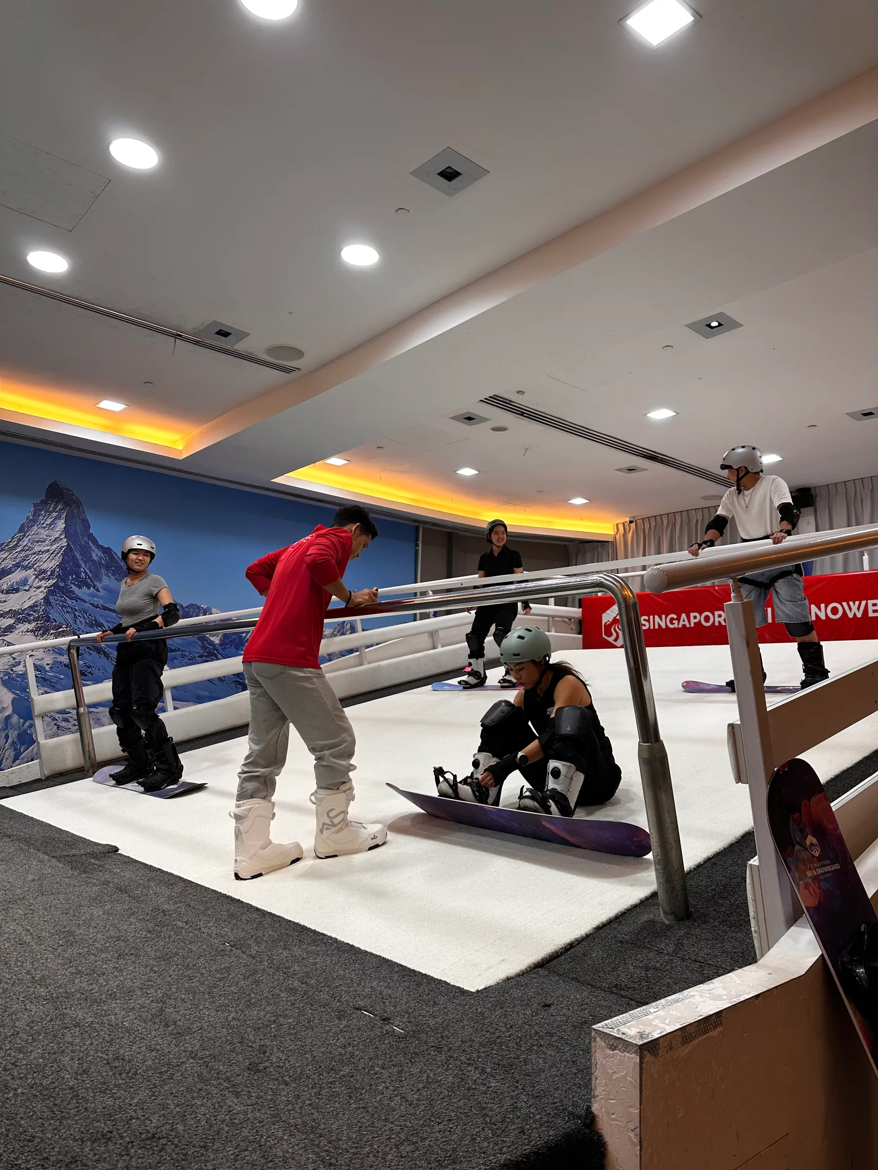 Snowboarders preparing their equipment with an instructor on an indoor simulator slope