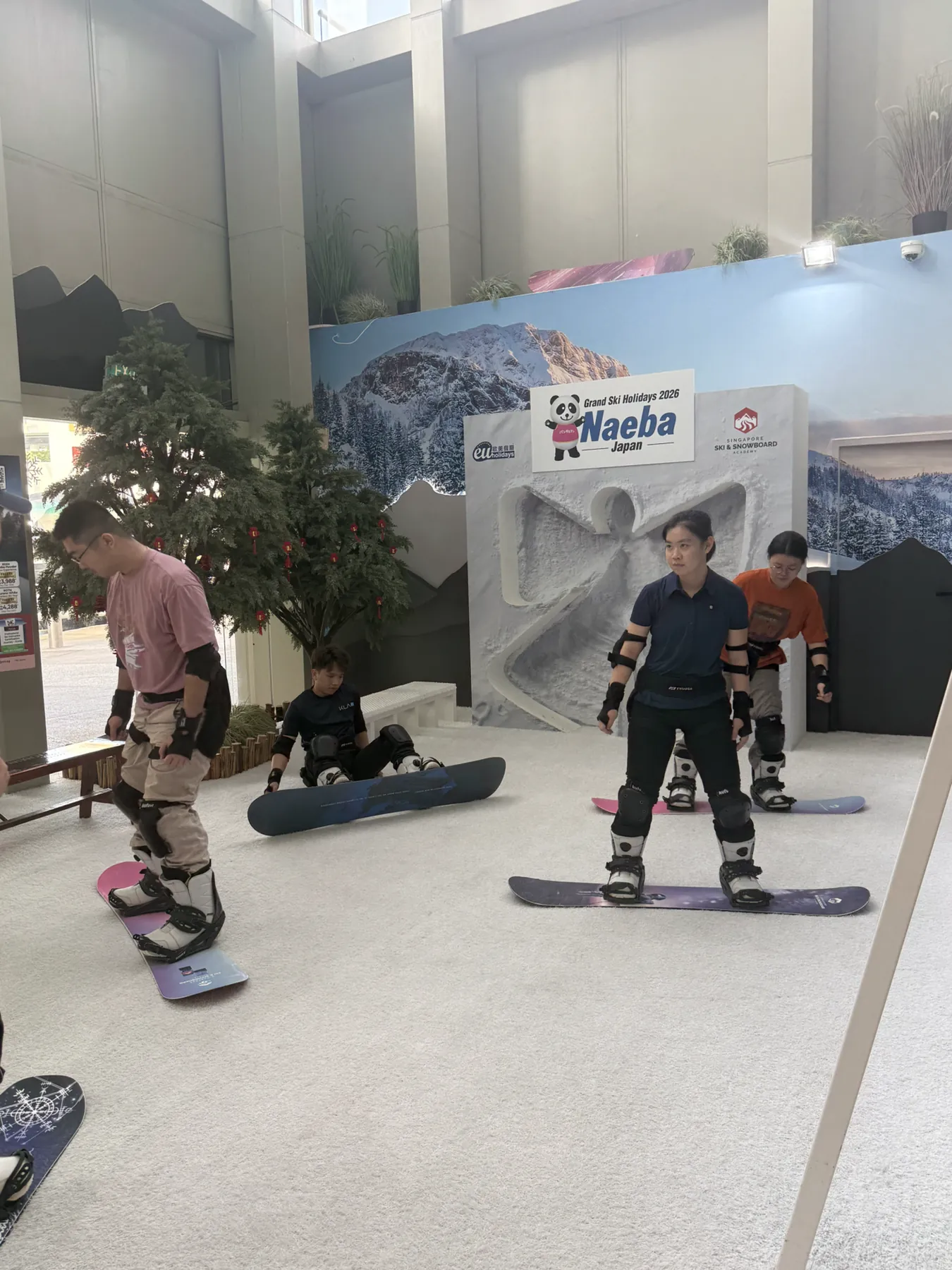 Participants wearing snowboards preparing beside an indoor training simulator