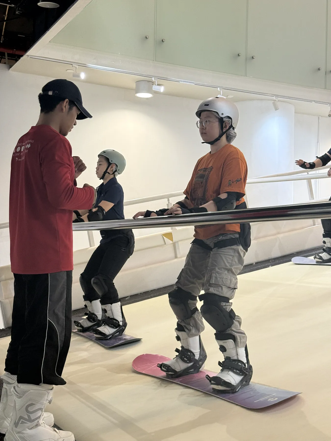 An instructor speaking with two participants wearing snowboards during indoor training