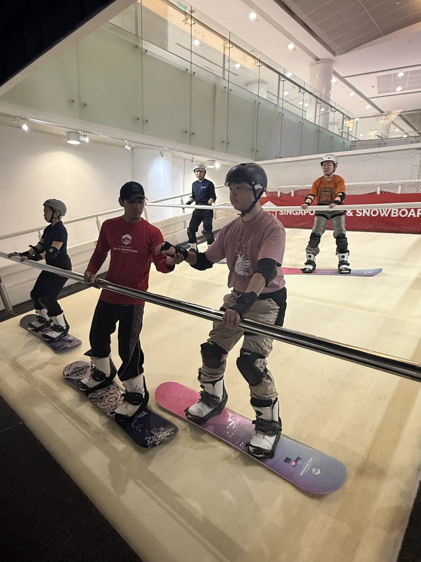 An instructor coaching a line of participants on the indoor snowboard simulator
