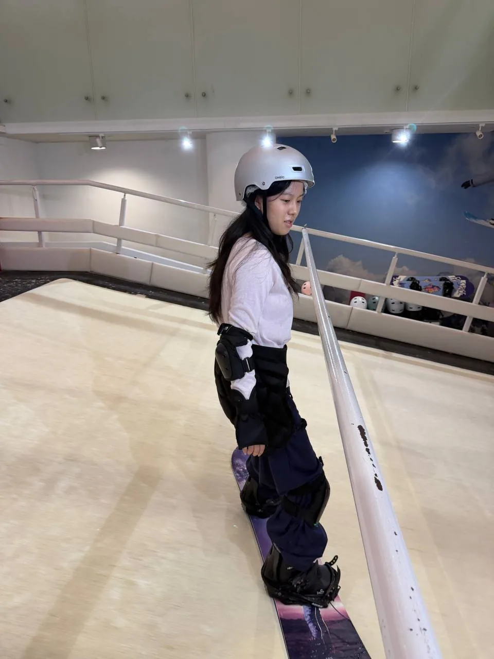 A snowboarder practising balance beside the support rail on an indoor training slope