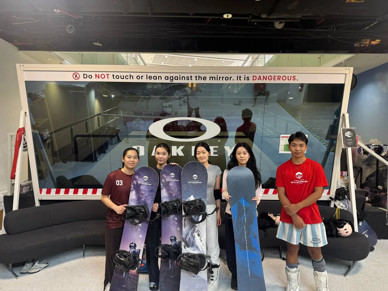 Four snowboarders and an instructor posing with snowboards after a weekly training session