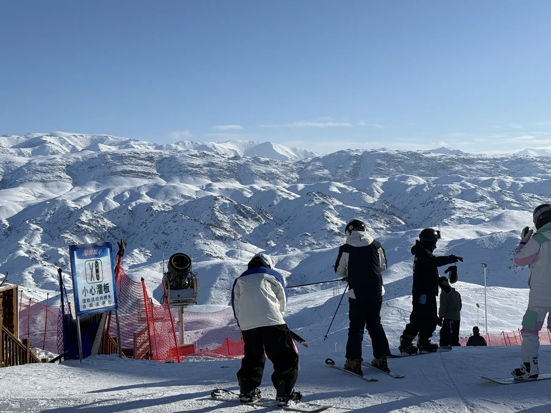 Skiers and snowboarders looking across snow-covered mountains from a viewpoint in Xinjiang